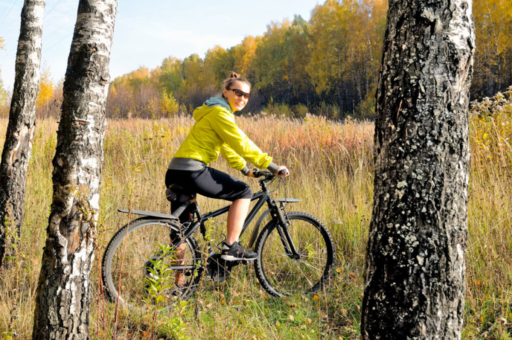 Young slim athletic girl on a bicycle in the autumn birch forest. Girl with a bicycle among birches with yellow leaves